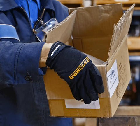 Person wearing box handling work gloves with extreme grip and performance fit holding a cardboard box in a warehouse.