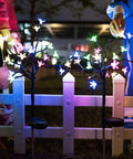 Two Pack Cherry Blossom Solar Garden Lights outdoor waterproof decor lamps glowing in yard at night near white fence