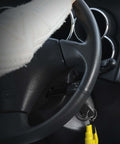 Resqme emergency keychain tool, yellow 2-in-1 seatbelt cutter and window breaker, attached to car keys near ignition.