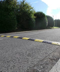 Eco XPT Speed Bump Kit With Cable Channel For Private Roads And Parking Lots Heavy Duty Plastic Rubber Reflective Black Yellow Modular 96 Inch Traffic Hump For Asphalt And Concrete Includes Mounting Hardware visible on paved road.