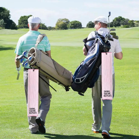 Two golfers walking with bags adorned with Swing Swear Repeat Embroidered Pink Golf Towel With Clip For Golf Bags Funny Ladies Golf Towel Perfect Gift For Moms Grandma Sister Aunt Golfer Retirement Birthday Mothers Day Sport Lover on a sunny course.