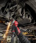Milwaukee 12V cut-off tool, red cordless tool, being used under a vehicle with sparks.