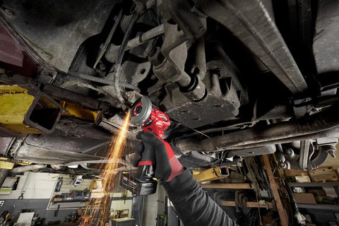 Milwaukee 12V cut-off tool, red cordless tool, being used under a vehicle with sparks.