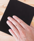 Hand resting on black sandpaper sheet from Top Notch Wet And Dry Sandpaper Assortment Pack With 60 To 320 Grit Sheets.