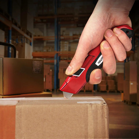 Auto Retracting Utility Knife With Dual Safety System For Fast Box Cutting Blade Auto Retracts When Off The Cutting Surface No Brainer Safety Push Button Release Easy Grip Handle Ideal For DIY Packing And Heavy Duty Work. Red metal utility knife cutting a sealed cardboard box in a warehouse