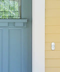 Wireless Doorbell 9 Series With Push Button Blue Grey Portable Chime Adjustable Volume MP3 Download Sleep Mode And Mute 8 Chimes At 90 dB Wall Mount Or Portable Up To 450 Feet Range 5 Year Battery Life installed on wall next to blue door.