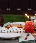 Colorful glass pineapple-shaped torches on outdoor dining table, demonstrating the 65 Inch Glass Pineapple Outdoor Torch With Copper Finish, Mosquito Repellent Torch For Yard And Garden, Integrated Snuffer, Burns Up To 15 Hours Per Fill, Use With Bite Fighter Torch Fuel, Patio Table Lighting That Stays Lit.