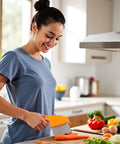 Side view of orange vegetable crinkle cutter with stainless steel blades slicing carrot on a cutting board.