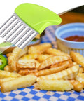 Green-handled stainless steel crinkle cutter with a wavy blade over a plate of french fries