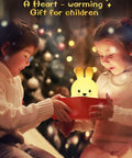 Kids opening a gift with Kids Night Light With Remote, 7 Color Kawaii Cat Nursery Lamp glowing softly, holiday setting.