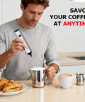 Man using Rechargeable Milk Frother With Stand 3 Speed Handheld Electric Wand Mixer For Matcha Lattes And Cappuccinos Dual Spring Whisk USB C Fast Charge Kitchen Must Have Gift For Home Baristas next to croissants and coffee on kitchen counter.