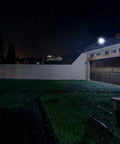 JUDYSSY Solar Flood Lights Led Floodlight 100W illuminating a dark garden area at night with bright light.