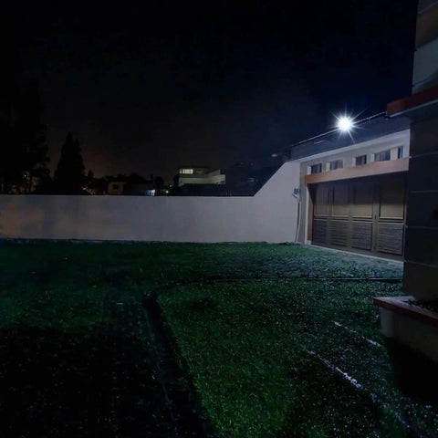 JUDYSSY Solar Flood Lights Led Floodlight 100W illuminating a dark garden area at night with bright light.