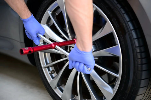 Person using LugStrong 26 Inch Universal Compact Lug Wrench Set for roadside tire change on a car with alloy wheels