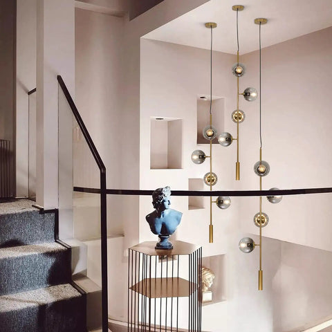 Lit Four Light Smoky Gray Glass Globe Pendant Light With Adjustable Cord And Gold Accents For Kitchen Island Bar Modern LED Chandelier Mid Century Industrial Ceiling Fixture hanging in a modern staircase area.