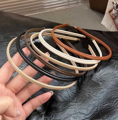 Five piece set of Premium Skinny Leather Headbands For Women in neutral shades held in hand, soft top grain leather accessories.