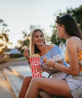 Two women sitting outdoors sharing popcorn from Heavy Duty Paper Popcorn Bags 1 Oz Individual Servings 500 Pack For Popcorn Machines