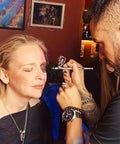 Makeup artist using Ultra Quiet Airbrush Compressor With Built In Air Tank Portable Lightweight 5.5lb Unit on model's face