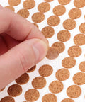 Hand holding a 3 8 inch round cork furniture pad from a sheet of 2000 Piece Self Adhesive Felt Furniture Pads.