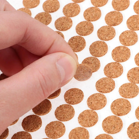 Hand holding a 3 8 inch round cork furniture pad from a sheet of 2000 Piece Self Adhesive Felt Furniture Pads.