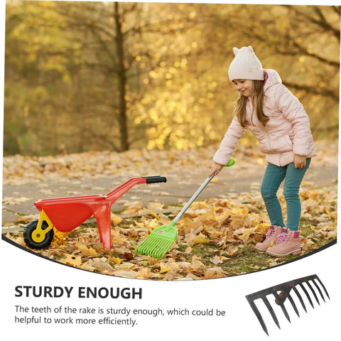 Child playing with a toy rake and wheelbarrow on a leaf-covered path in autumn.