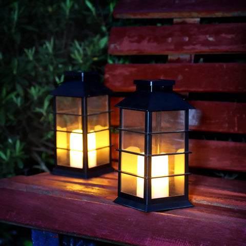 Two Pack Lit Solar Powered Outdoor Hanging Lanterns With Waterproof LED Flickering Flameless Candles, black on bench at night