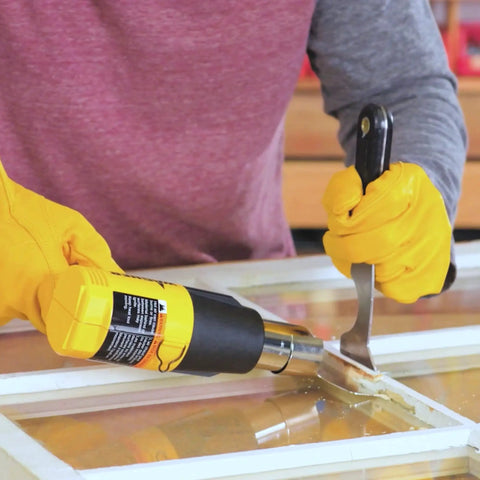 Person using Dual Temp Heat Gun Kit With 750 Degrees F And 1000 Degrees F, Three Nozzles Included, DIY-Friendly For Home Projects, Ideal For Shrink Wrap, Softening Paint, Bending Plastic Pipes, Loosening Rusted Bolts And More to remove paint from a window frame.