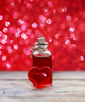 Glass bottle with red liquid and cork top next to heart-shaped gemstone on wooden surface against a bokeh red background