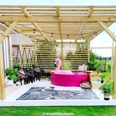 Outdoor pergola with chairs, pink tub, and greenery, decorated with 48 Ft Soft Warm White Outdoor String Lights With Shatterproof Acrylic Bulbs, creating cozy vibe.