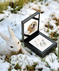 Paw Print Keepsake Kit For Dogs And Cats in black leather display, on snow with ceramic rabbit.