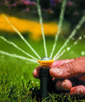 Close-up of hand adjusting High Efficiency Pro Rotary Sprinkler With Built In Regulator Delivers Constant 30 PSI, spraying water in lawn