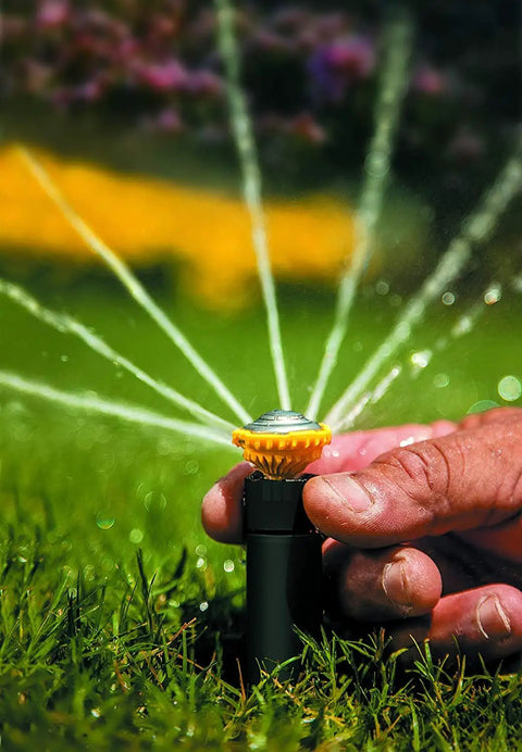 Close-up of hand adjusting High Efficiency Pro Rotary Sprinkler With Built In Regulator Delivers Constant 30 PSI, spraying water in lawn