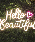 Hello Beautiful Neon Sign For Girl's Room Wall Decor With Dimmer Switch Romantic Neon Light For Weddings Valentine's Day Parties Gifts 12V Warm White With Power Adapter Included glowing on a green leaf wall.