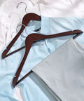 Solid Wood Hangers 20 Pack With Smooth Walnut Finish Non Slip Pant Bar 360 Degree Swivel Hook holding blue shirt and pants