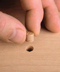 Heavy Duty Self Centering Plug Cutter Set Packing Three Slick Blades For Clean Door Holes With Fast Grip Shank and Rock Solid Hardened Steel Design Loaded With A Sweet Storage Case For Easy Shop Access, hand placing wooden plug into hole.