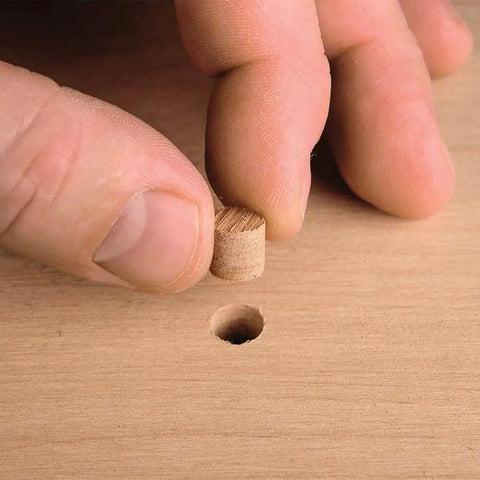 Heavy Duty Self Centering Plug Cutter Set Packing Three Slick Blades For Clean Door Holes With Fast Grip Shank and Rock Solid Hardened Steel Design Loaded With A Sweet Storage Case For Easy Shop Access, hand placing wooden plug into hole.