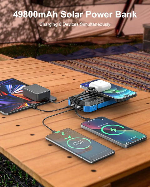 Massive 49800mAh Solar Power Bank with Wireless Charging and cables charging multiple devices on a wooden table