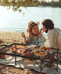 Couple enjoying picnic on beach with tool free foldable outdoor table with wing panels and mesh desktop, 3x2 ft.