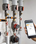 HVAC In-Pipe Temperature Probe With Bluetooth App displays readings on smartphone beside heating system pipes.