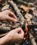 Person using All In One Multitool Lighter Keychain With Bottle Opener, Reusable Waterproof Fire Starter For Outdoor Survival near campfire.