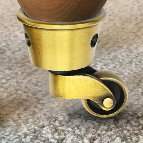 Close-up of a vintage zinc alloy swivel caster with 1-3/4 inch OD, antique brass bronze finish, attached to furniture leg.