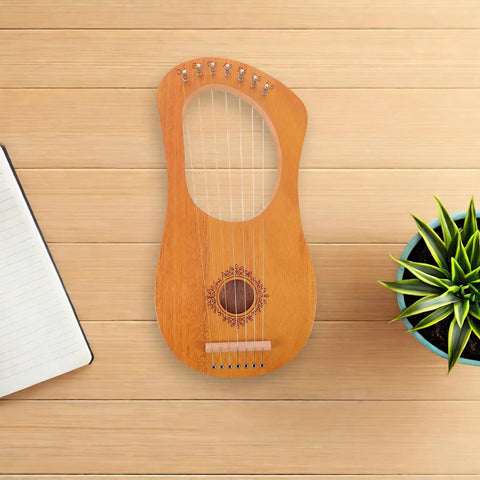 Top view of Portable 7-String Lyre Harp Kit For Adults With Wooden Body and metal strings, on wooden surface next to notebook and plant.