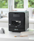 Top Shelf Home Coffee Roaster Machine With Fast Quartz Heating And Ultra Quiet Chaff System For Smooth Daily Roasting In A Sleek Matte Black Cabinet on a kitchen counter.