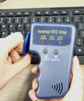 Hands using Portable No Fuss Handheld 125KHz RFID Reader Writer Copier for T5577 and EM4305 Smart ID Card Duplicator near keyboard