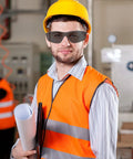 Construction worker wearing Clear ANSI Z87.1 Safety Glasses For Work, Lab, And Construction, holding blueprints, in a high-vis vest and hard hat.