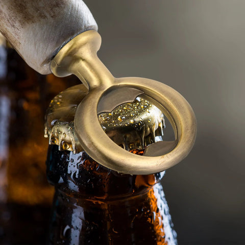 Close-up of brass-colored metal bottle opener ring on a beer bottle neck; DIY wedding hardware.