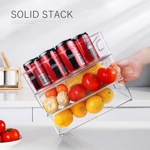 Hand holding Stackable Fridge Organizer Bins Set Of 6 Clear Kitchen Storage Bins With Easy Grip Handles, filled with fruits and cans.