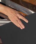 Hand placing a sheet of grey sandpaper on a wooden surface, part of the Get The Ultimate Multipurpose Sandpaper Set With 10 Sheets Of Assorted Grits.