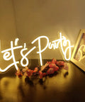 Lets Party Neon Sign Dimmable LED Neon Light For Wall Decor 16x7 Inches Word Sign glowing warmly on a table with flowers