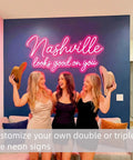 Three women smiling in front of "Nashville looks good on you" pink Personalized Neon Sign For Weddings And Events Dope Custom LED Light Sign With Your Name Or Logo For Bars Salons Offices And Lounges In 16 To 60 Inches Ready To Impress